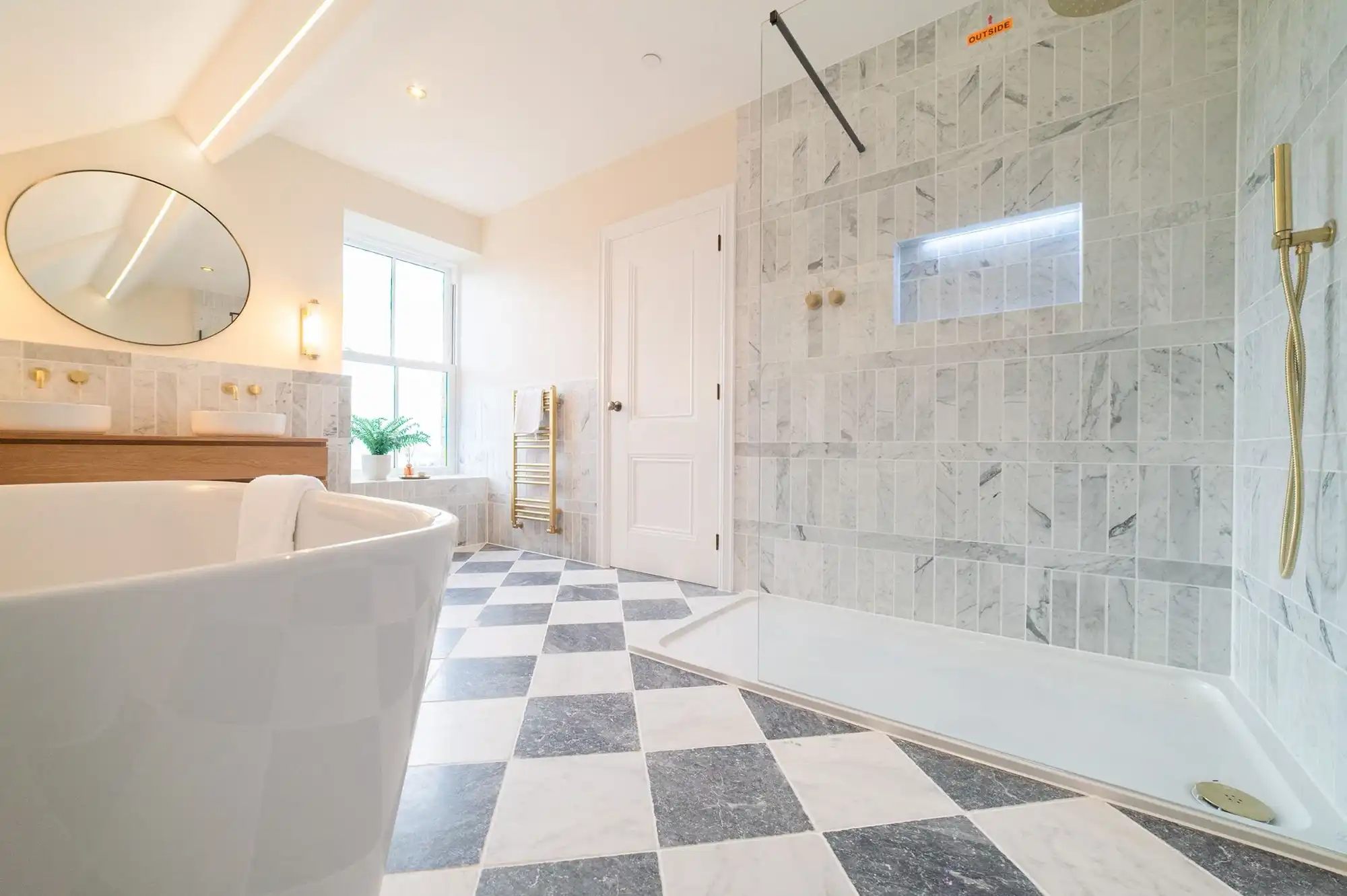 Modern bathroom featuring a freestanding white tub, double sink vanity, glass shower, and checkerboard flooring in black and white tiles.