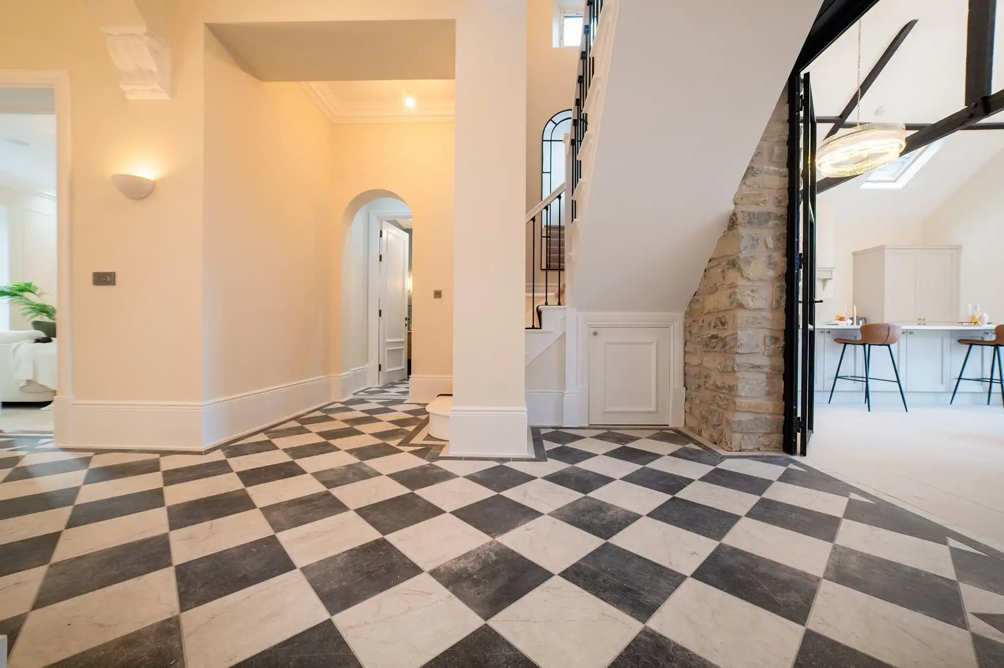 Modern entryway with a checkered floor, staircase, and archway. Soft lighting and a stone accent wall create an inviting atmosphere.