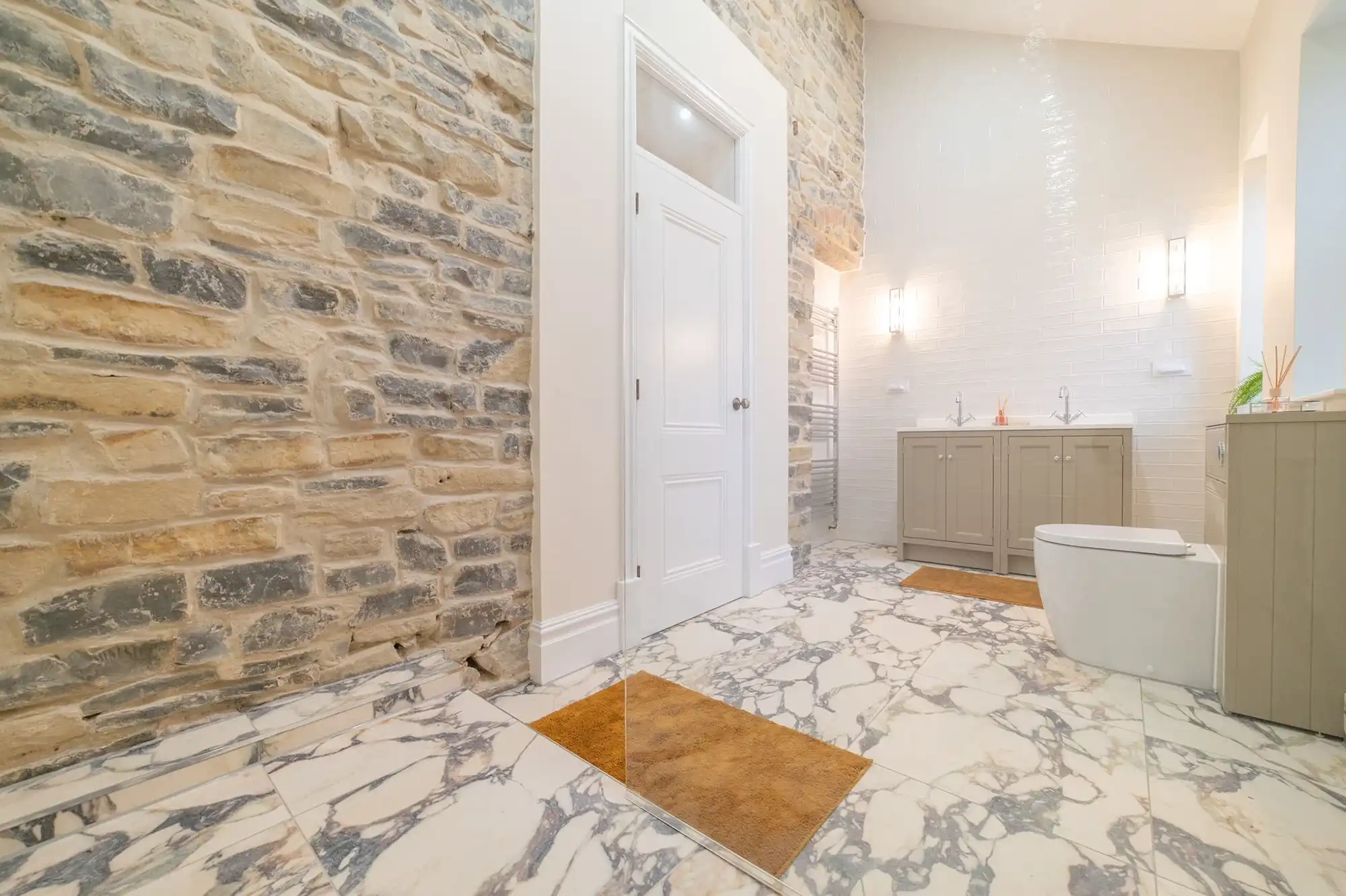 Modern bathroom featuring a stone wall, marble floor, double sink vanity, and contemporary fixtures with warm lighting.